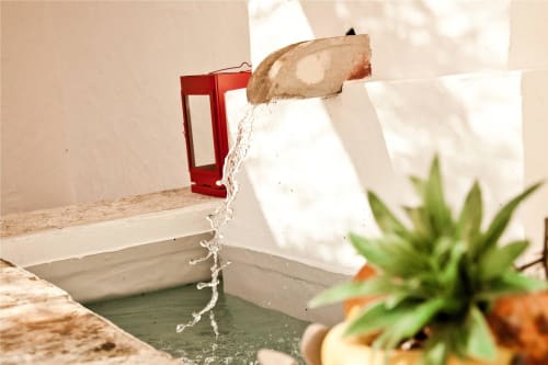 Água fluindo de uma torneira rústica para uma bacia em Casas de Juromenha, Portugal, com planta em vaso próxima
