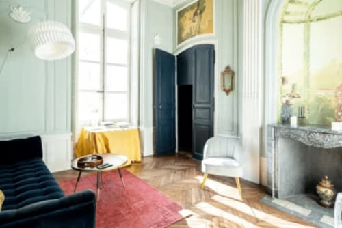 Élégante chambre de l'Hôtel Henri II au Mans avec portes bleues, cheminée, canapé bleu marine et lumière naturelle par hautes fenêtres