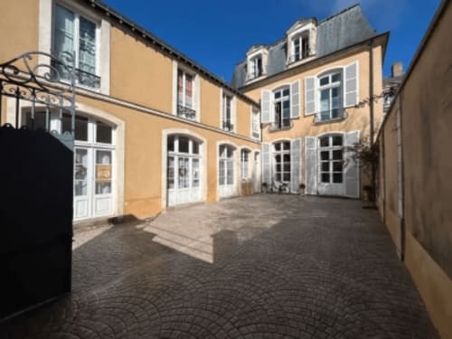 Cour de l'Hôtel Henri II au Mans avec bâtiment historique jaune, portes blanches et pavage en pierre