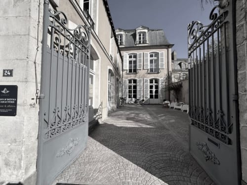 Elegant courtyard entrance of Henri II Hotel in Le Mans, France with ornate iron gates and classic architecture