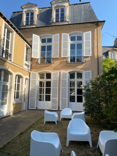 Henri II hotel courtyard in Le Mans with yellow facade, white shutters, and modern seating area