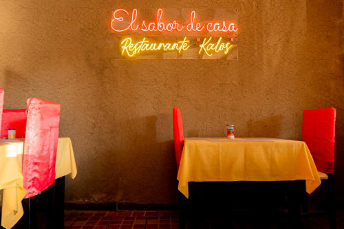 Interior del restaurante El sabor de casa con letreros de neón, mesas coloridas y decoración rústica en Hotel Makarios en Tuxtla