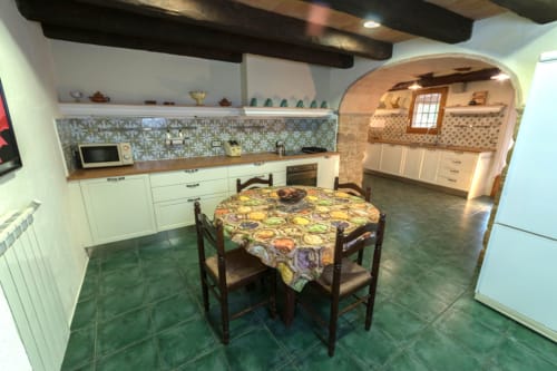 Amplia cocina rústica con muebles crema, salpicadero de azulejos estampados, mesa de comedor con mantel colorido