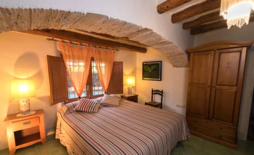 Dormitorio acogedor en el casarón Can Gat Vell de Girona con ropa de cama a rayas, vigas de madera y vistas al jardín