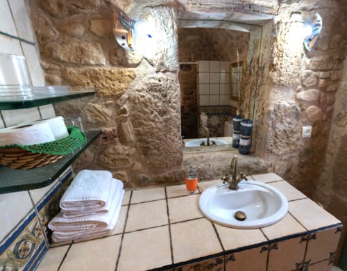 Baño rústico de piedra en la casa rural Can Gat Vell de Girona con lavamanos redondo, toallas y baldosas tradicionales