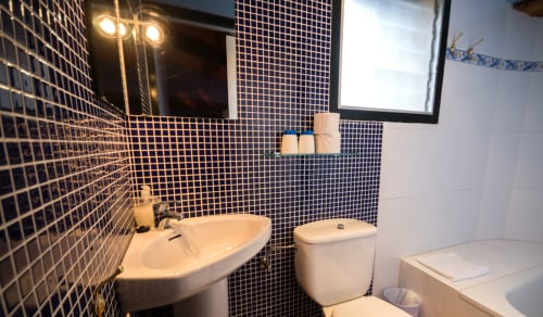 Baño moderno con paredes de azulejos oscuros, lavabo blanco, inodoro y bañera en la casa rural Can Gat Vell en Girona