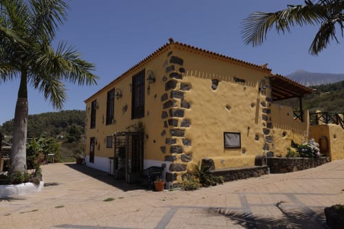 Casita amarilla con detalles de piedra en Casonas de Marengo en Icod de los Vinos, rodeada de palmeras y montañas