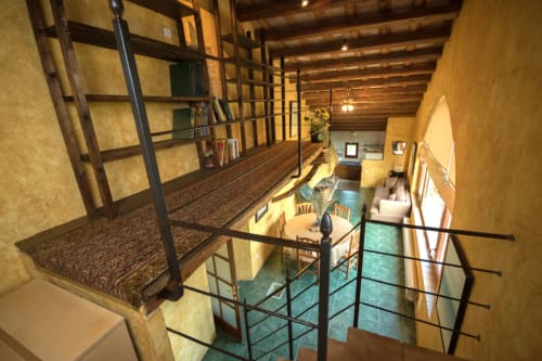 Dormitorio en altillo de la casa rural Can Gat Vell con vigas de madera y barandilla con vistas al jardín y comedor
