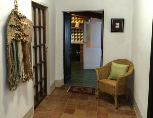 Entrada de la casa rural Can Gat Vell en Girona con silla de mimbre, borla decorativa y puertas de madera hacia la sala de estar
