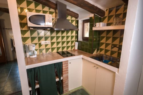 Cocina retro verde y beige con azulejos geométricos, encimeras de madera, microondas y estanterías abiertas en Can Gat Vell