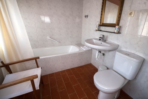 Baño con sanitarios blancos, suelo de terracota, bañera, lavabo e inodoro en la casa rural Can Gat Vell en Girona