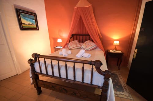 Dormitorio romántico con dosel rojo en la casita Can Gat Vell, Girona, cama de madera, iluminación cálida y decoración tradicional