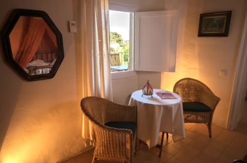 Acogedora sala de estar con sillones de mimbre en pequeña mesa, espejo, puertas abiertas a terraza con vistas a la ciudad en Can Gat Vell, Girona