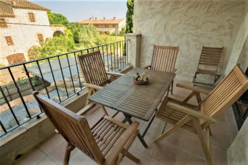 Terraza con mesa de comedor y sillas de madera con vistas a la campiña de Girona en la casa rural Can Gat Vell en Empordà