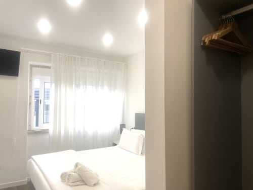 Modern bedroom at Vila Alexandra hostel in Costa da Caparica with white bed, TV, window with city view, and open closet with