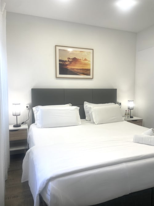 Modern bedroom at Vila Alexandra hostel in Costa da Caparica with white bedding, gray headboard, and sunset artwork