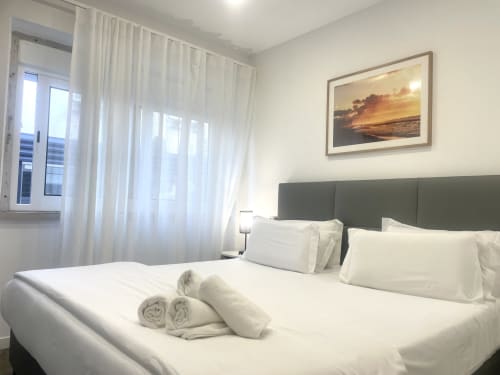 Modern bedroom at Vila Alexandra hostel in Costa da Caparica with green headboard, white bedding, and sunset artwork on wall