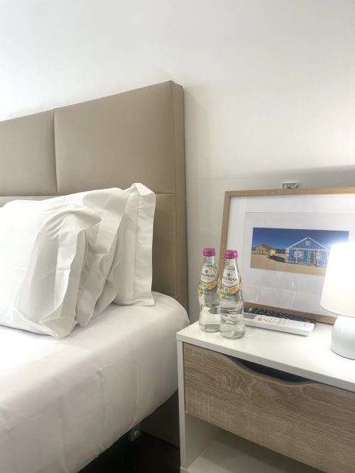 Praia Princesa room at Vila Alexandra hostel in Costa da Caparica with bed, bedside table, water bottles, and framed beach