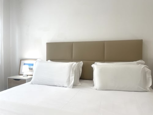 Clean modern bedroom at Vila Alexandra hostel in Costa da Caparica with white bedding, olive headboard, and minimalist decor