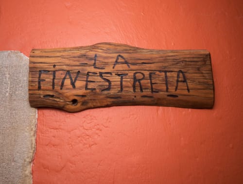 Rústico letrero de madera « LA FINESTRELLA » grabado en madera contra pared color coral en el alojamiento Can Gat Vell en Girona