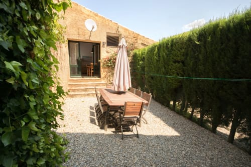 Cabaña rústica de piedra con terraza de comedor al aire libre, sombrilla y frondosos setos verdes en Empordà, Cataluña