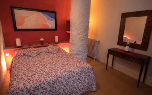 Dormitorio acogedor con paredes rojas, edredón estampado, chimenea y vistas al jardín en la casa rural Can Gat Vell de Girona