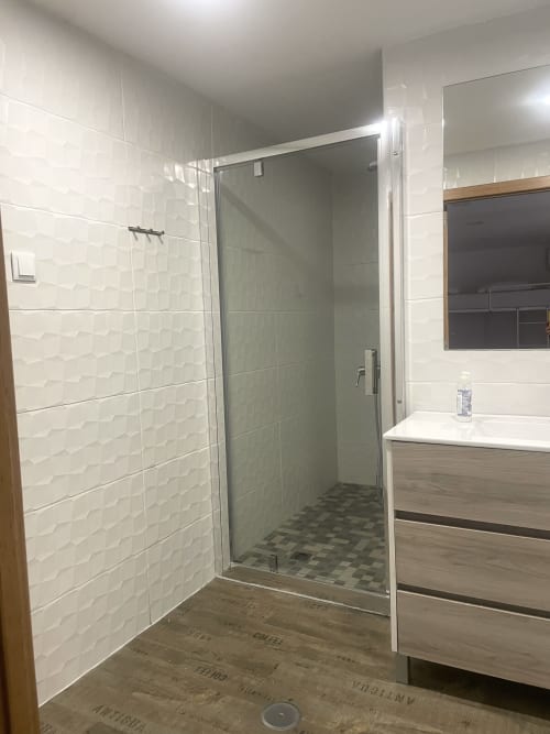 Modern bathroom with glass shower enclosure, white textured tiles, and vanity sink at Vila Alexandra hostel, Costa da