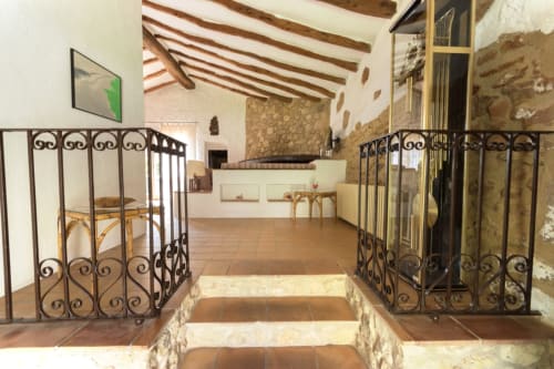 Escalera de piedra rústica con puertas de hierro forjado hacia alojamiento luminoso en Can Gat Vell, casa rural familiar
