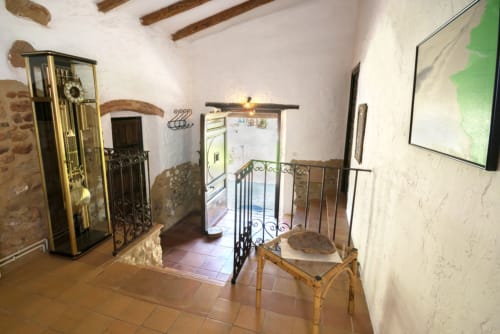 Interior de casa de piedra histórica con vigas de madera, barandilla de hierro forjado y muebles rústicos en Can Gat Vell, Girona