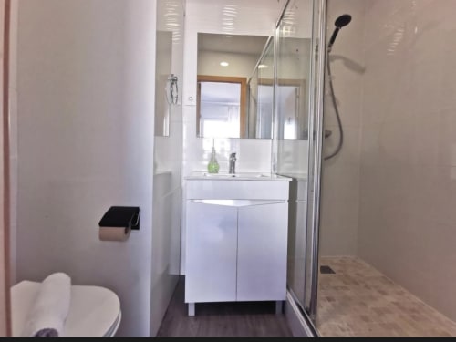 Modern bathroom in Room 13 at Vila Alexandra hostel, Costa da Caparica with white vanity, glass shower, and toilet