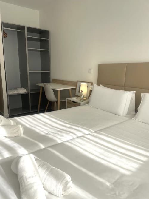 Bright modern bedroom at Vila Alexandra hostel in Costa da Caparica with twin beds, desk, and open wardrobe