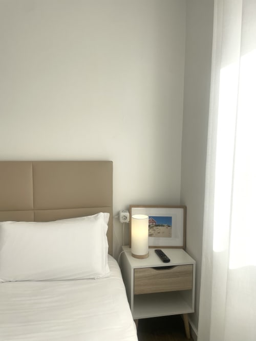 Bright minimalist bedroom at Vila Alexandra hostel in Costa da Caparica with white bedding, beige headboard, and bedside