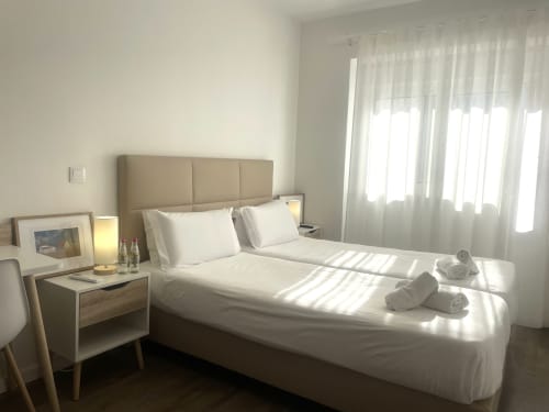 Modern bedroom at Vila Alexandra hostel in Costa da Caparica with white bedding, beige headboard, and bright windows