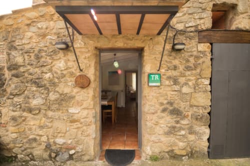 Entrada de casa de piedra en Can Gat Vell, Girona. Puerta de terracota con señal de salida verde y marquesina.