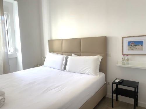 Modern bedroom at Vila Alexandra hostel in Costa da Caparica with beige headboard, white linens, and city view