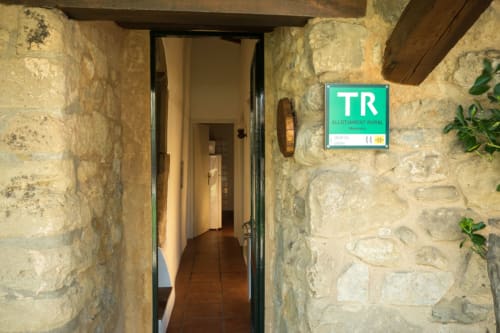 Entrada de casa de piedra con cartel verde de alojamiento rural TR, Girona, Cataluña
