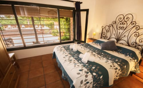 Dormitorio luminoso con dos camas, cabecero de hierro forjado decorativo y balcón con vistas a la piscina