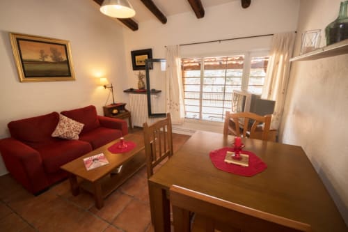 Acogedora sala de estar y comedor de la casa rural Can Gat Vell, Girona, con sofá rojo, mesa de madera y vistas al jardín