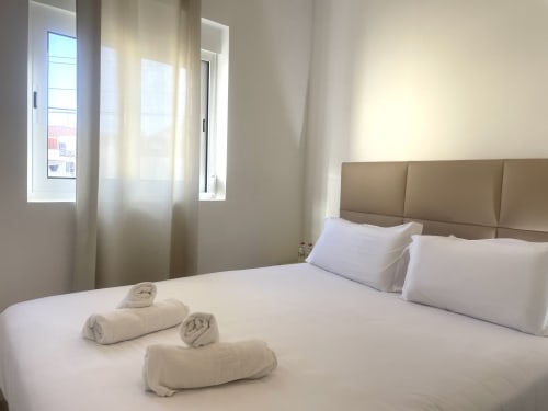 Modern bedroom at Vila Alexandra hostel in Costa da Caparica with queen bed, taupe headboard, white linens, rolled towels,