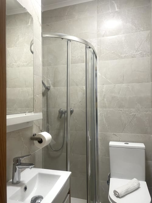 Modern bathroom at Vila Alexandra hostel in Costa da Caparica with marble tiles, curved glass shower enclosure, and white