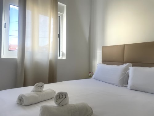 Clean bedroom at Vila Alexandra hostel in Costa da Caparica with taupe headboard, white bedding, rolled towels, and city