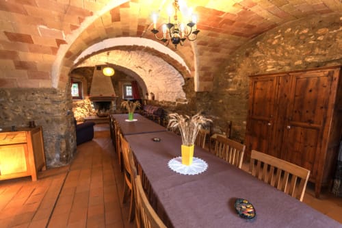 Comedor con bóveda de piedra y sillas de madera en la casita Can Gat Vell en Girona, con techo abovedado rústico de ladrillo