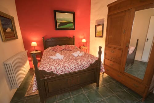 Dormitorio con cama de madera, paredes rojas, iluminación cálida, armario y vistas al jardín en la casa rural Can Gat Vell en Girona