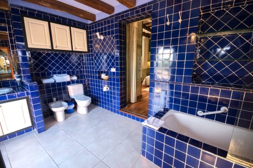 Baño de lujo con paredes de azulejos azul intenso, bañera, doble lavamanos e inodoro en la casa rural Can Gat Vell en Girona
