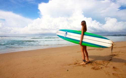 Surfer holding green and white surfboard on sandy beach at Costa da Caparica near Vila Alexandra hostel