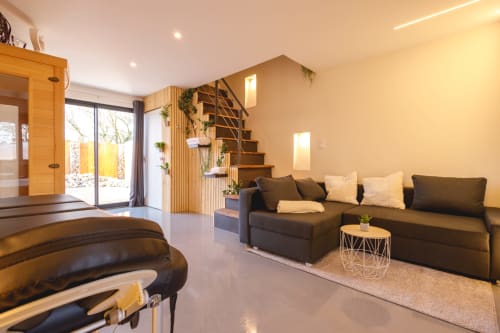 Salon moderne de la villa au Domaine du Haut de la Dombes avec canapé foncé, étagères en bois et portes donnant sur le jardin