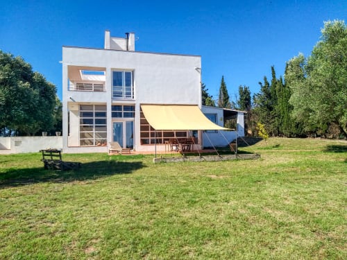 Casa blanca moderna con toldo amarillo en Palafrugell, España, con jardín bien cuidado y cipreses