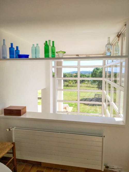 Sala luminosa con estanterías de cristalería de colores, caja de madera, con vistas a campos verdes y montañas en Palafrugell