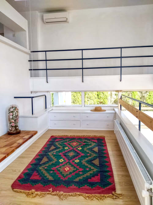 Luminoso dormitorio en mezzanine de Finques Garcia Enrich con alfombra geométrica, almacenaje blanco, barandillas azul marino y vistas al jardín