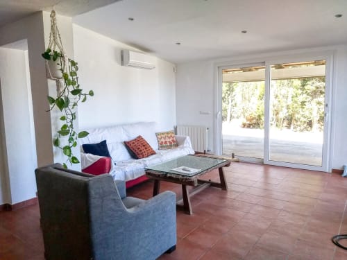 Salón luminoso en Finques Garcia Enrich en Palafrugell con sofá, sillón, mesita de café y puertas de cristal con vistas